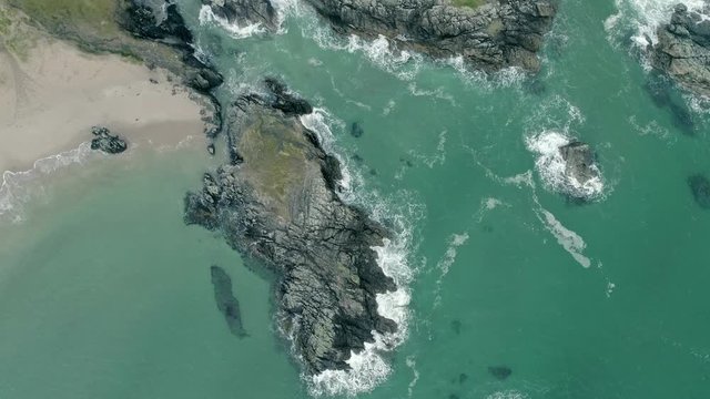 Aerial shot tracking high and topdown forward over a stunning craggy rocky outcrop off of the Durness coastline known as Sango Sands in Scotland. Amazing turquoise tropical water.