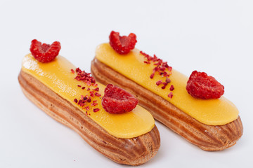Set of delicious eclairs with yellow glaze and raspberries