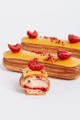 Set of delicious eclairs with yellow glaze and raspberries