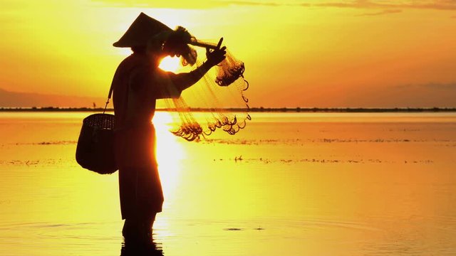 Silhouette of a Balinese fisherman casting a traditional fishing net at sunrise
