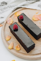 Two pieces of chocolate cake on wooden board decorated with floral petals