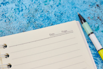 Notebook, pen, on blue abstract background. horizontal view from above. white piece of paper. angular placement of the object.