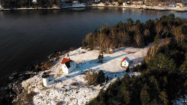 Aerial ORBIT over a snow covered Curtis Island Lighthouse at sunrise with long shadows in the snow