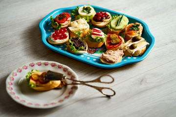 old blue tray with a set of healthy tapas or mini sandwiches with food tongs on a light wooden table