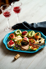 set of mini sandwiches or tapas for two with glasses of wine on a light wooden table