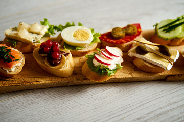 wooden board with colorful healthy mini sandwiches or tapas on a light wooden table