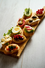 wooden board with colorful healthy mini sandwiches or tapas on a light wooden table