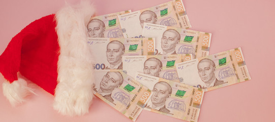 Ukrainian hryvnia banknotes coming out of Santa Claus hat on a pink background. Christmas Shopping Concept