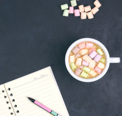 Cup with coffee and marshmallows, blank open notebook with pen on abstract black background. View from above. Flat layout. space for text. hot drink.