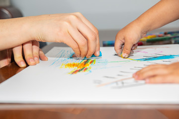 Hands of mom and son drawing together with colorful crayons