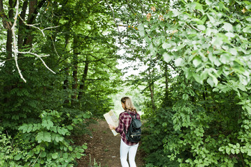Naklejka na ściany i meble Portrait of a young beautiful blond woman in tartan shirt holding a map in the forest.