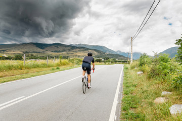 A cyclist riding towards storm clouds above mountains