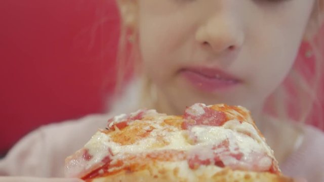 A young girl with plaits is eating a piece of pizza. Charming happy young girl laugh and biting off big slice of fresh made pizza. International food concept. Close up.