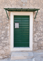 Fototapeta na wymiar Green wooden doors with silver mailbox on a stone house. Exterior architectural details.