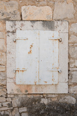 Very old closed window with white wooden shutters. Window with stone frame on a stone house.