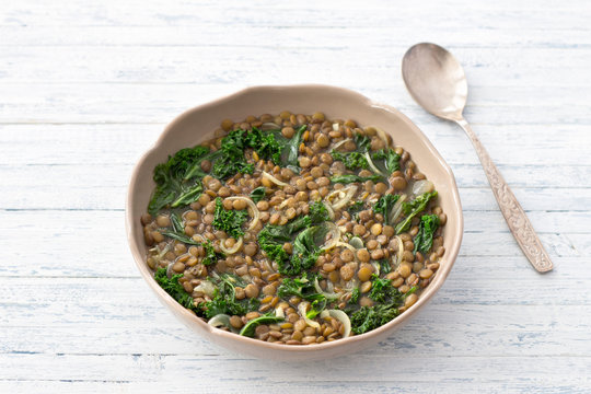 Stewed kale lentils with onions and garlic on a light background, selective focus, free space. Delicious homemade healthy food