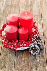 Four candles in a white wreath with red berries on a wooden rustic background with lights. advent...