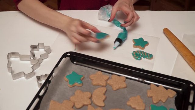 Girl decorates homemade gingerbread cookies with colored glaze close up. Christmas baking.