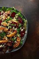 Grilled quince salad with baked and fresh grated beetroot, blue cheese, walnuts on rustic table