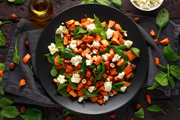Healthy roasted sweet potato salad with spinach, feta cheese, hazelnut nuts in black plate, rustic background
