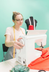 Sewing workshop. Seamstress at work. Young woman working with sewing machine on a colored background