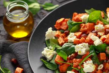 Healthy roasted sweet potato salad with spinach, feta cheese, hazelnut nuts in black plate, rustic background