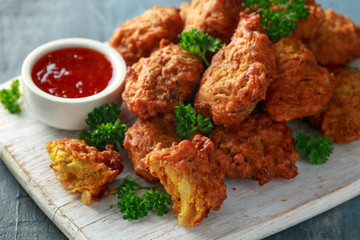 Crispy onion bhajis with sweet chilli sauce on white wooden board