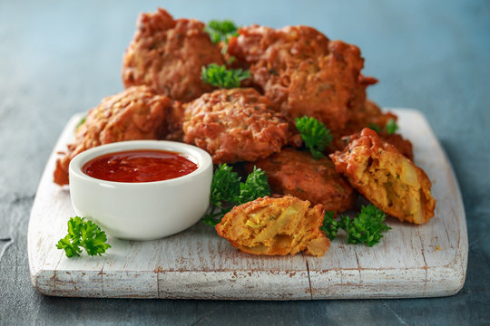 Crispy onion bhajis with sweet chilli sauce on white wooden board