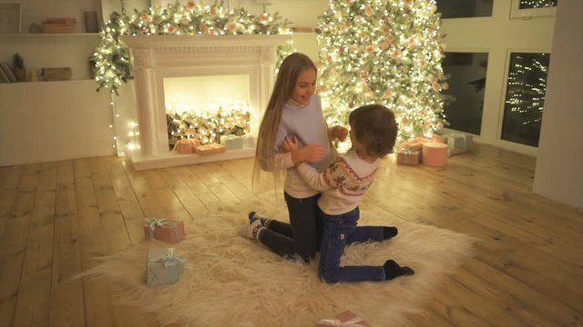 The kids tickling each other near the christmas tree. slow motion