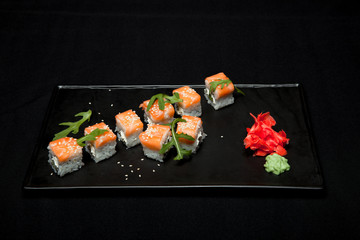 Sushi roll with salmon and avocado on plate on black background top view