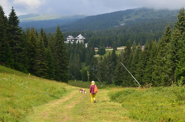 Woman dressed in royal stewart hiking with her dog - Cavalier King Charles Spaniel - on mountain...