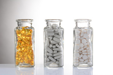 Three glass bottles with different pills on a light gray gradient