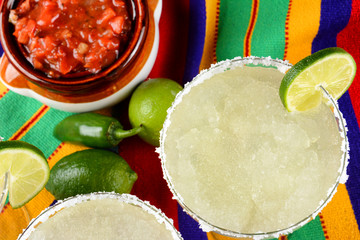 Margaritas and Salsa on a colorful  table cloth, with limes, and peppers.