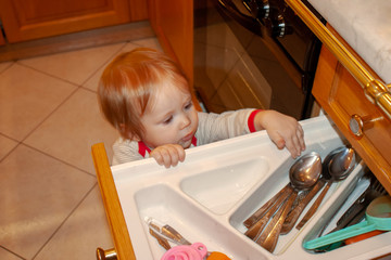 Baby is actively exploring the contents of kitchen box. Safety of the little explorer from unwanted objects and sharp corners, doors and drawers, to which, like a magnet, attracts the young know-all.