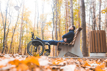 Young man resting sitting on a bench with his legs on his wheelchair.