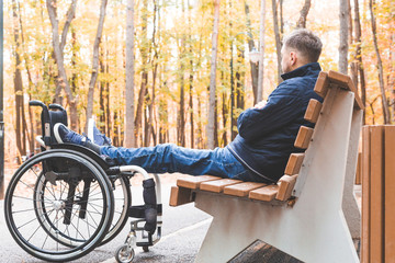 Young man resting sitting on a bench with his legs on his wheelchair.