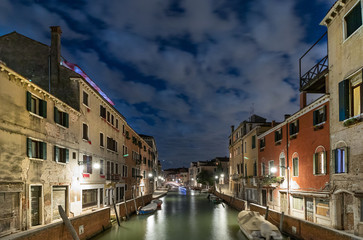 A narrow canal - street with boats in Venice at night, Italy.