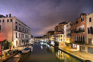 A canal - street with boats in Venice at night, Italy.