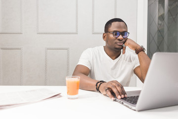 Young African American businessman working on a laptop in the kitchen in a modern interior.