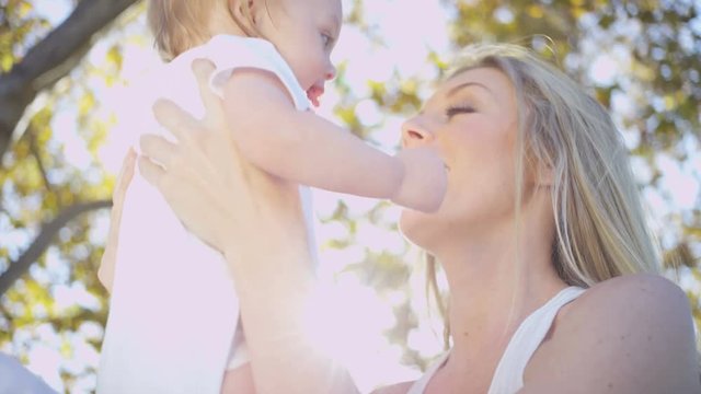Smiling beautiful blonde young European mum tenderly holding her baby daughter outdoors in the park 