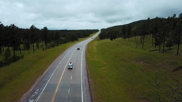 Static drone shot of traffic cars moving along concrete highway between wild green forest rocky hills on a cloudy day.