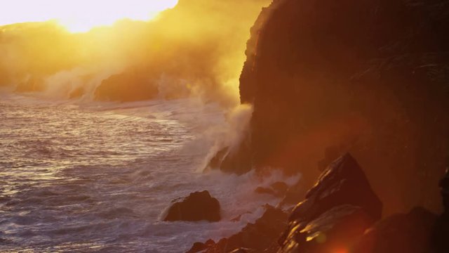 Red hot lava falling into ocean at sunrise causing rising steam seen from distance Hawaii Kilauea Big Island USA 