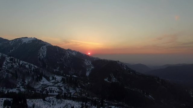 Aerial tracking slowly forward above the Shymbulak Ski Resort in the Medeu mountain range near the city of Almaty in Kazakhstan. Amazing sunset, perfect wintery scene.