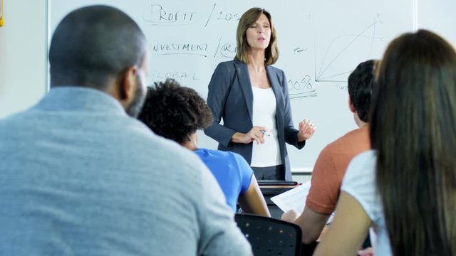 Ambitious Caucasian American female tutor teaching mature university students in modern classroom 