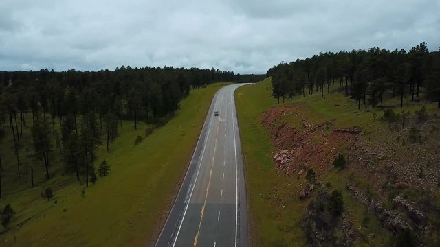 Beautiful aerial shot of traffic on highway road between wild clean green forest rocky hills with trees on overcast day.
