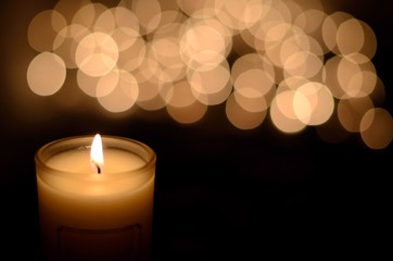 Candle with flame and bokeh light in dark background for praying in Church concept.