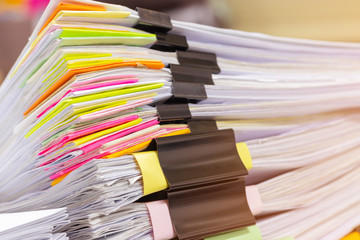 Close up pile of unfinished homework assignment stacked in archive with colorful papers and binder clip on table waiting to be managed and inspected. Stack of paperwork. Education and business concept