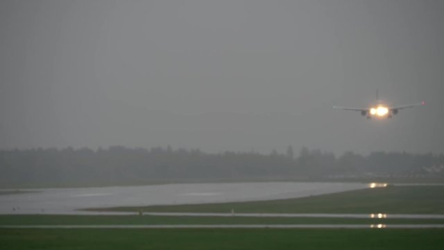 Wide shot of a jet plane coming in for a landing during a storm on a wet runway