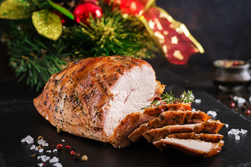 Roasted sliced Christmas ham of turkey on dark rustic background. Festival food.