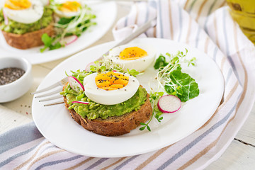 Healthy food. Breakfast. Avocado egg sandwich with whole grain bread on white wooden background.